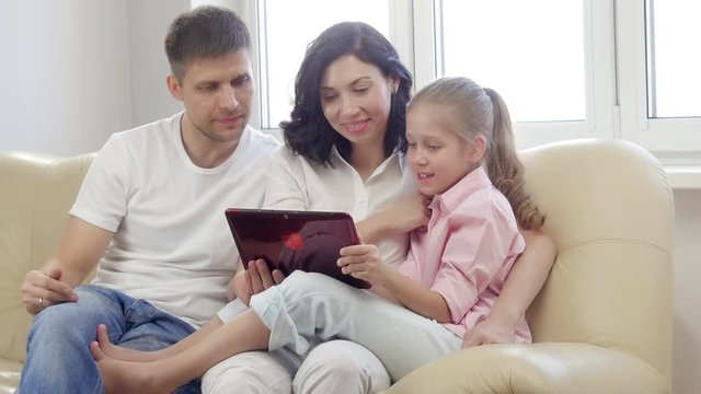 Parents showing digital tablet to their daughter at home.