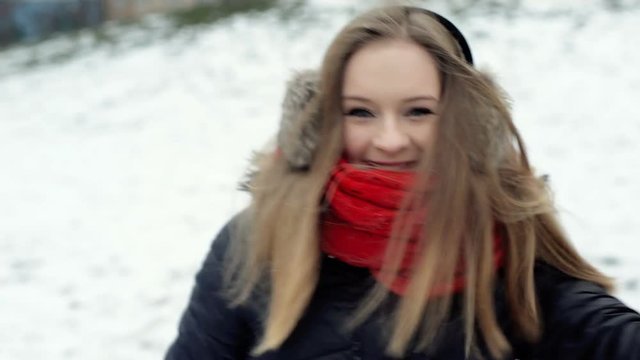 Happy girl running in the wintry park and throwing snowball to the camera, steadycam shot

