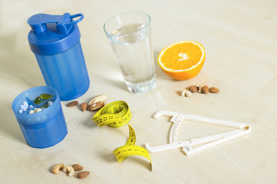 Fitness and healthy life concept. Fruits, water and nuts on a wooden table. Fitness equipment. Body fat caliper and measuring tape.