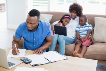 Worried man working while his wife play with kids 