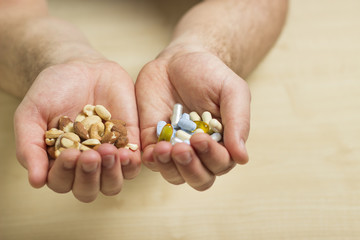 Man's hands holding a pile of healthy nuts and a pile of medication. Pharmacy pills in one hand and healthy walnuts and peanuts in the other hand.