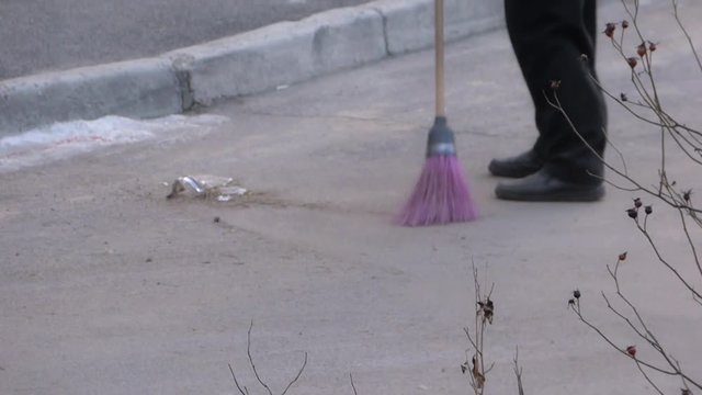 Winter day. Janitor with red broom sweeping the street
