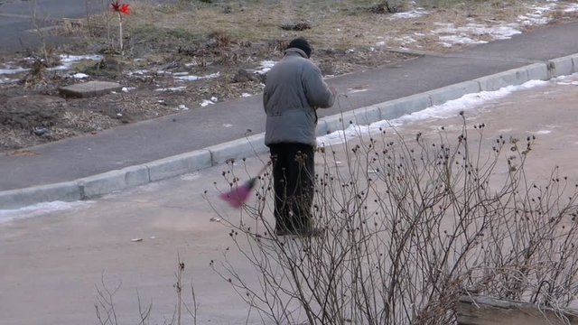 Winter day. Janitor with red broom sweeping the street