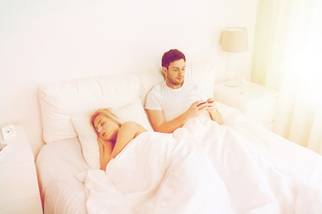 man texting message while woman is sleeping in bed