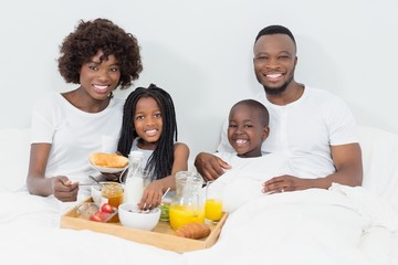 Portrait of smiling parents and kids having breakfast in bedroom