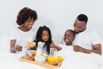 Obraz na płótnie Canvas Smiling parents and kids having breakfast in bedroom