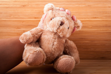 Teddy bear in hand on wooden table.
