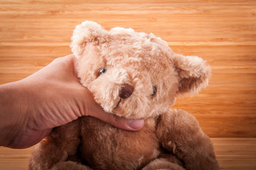 Teddy bear in hand on wooden table.