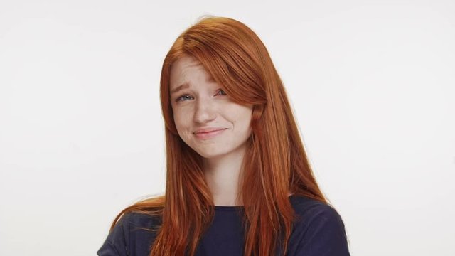 Not-impressed cute foxy Caucasian teenage girl wearing dark blue t-shirt lokking at camera smiling on white background in slowmotion