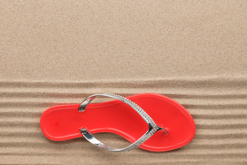Trendy red flip flops decorated with rhinestones, standing on the beach sand.