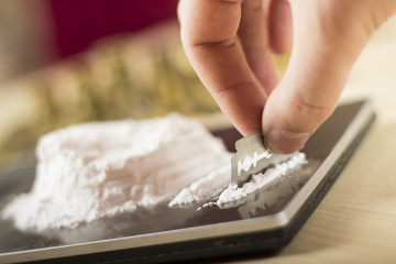 Close-up of a hand holding a razor blade. Making heroin lines on a digital scale. Drug dealer counting the drugs. Drugs and crime concept.