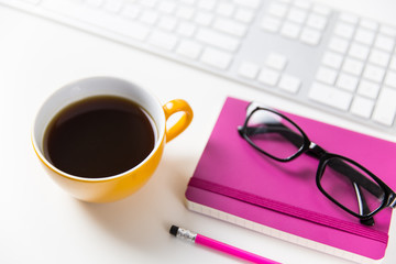 Coffee, glasses, notebook and computer keyboard on white desk