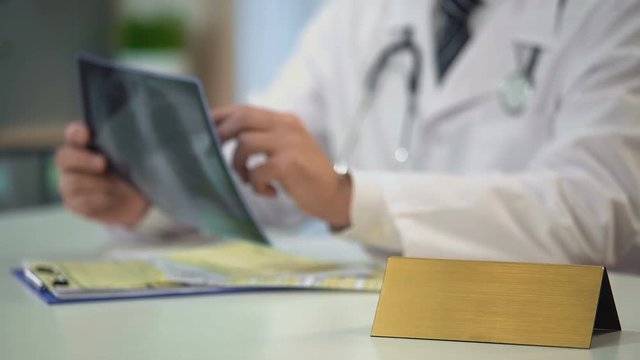 Male doctor looking at lungs x-ray, writing diagnosis, blank nameplate on table
