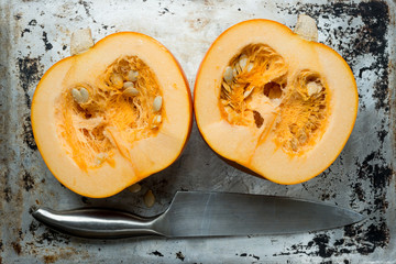 Pumpkin Halves and Kitchen Knife on Grunge Aluminium Surface