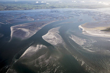 aerial view of the mudflat coastline at low tide with water winding in the mud and sand bank,...