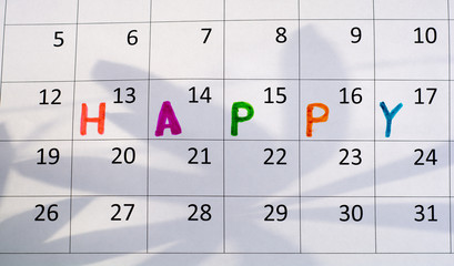 On the calendar sheet is written the word "happy." On the calendar page the shadow of the leaves of the plant.
