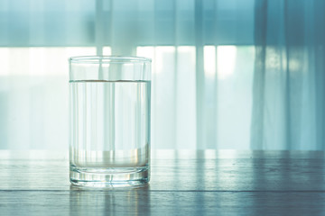 Glass of water on wooden table and light blurred background.