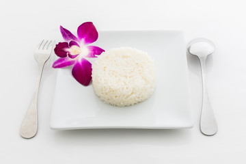 cooked rice with a spoon and fork on white dish and orchid