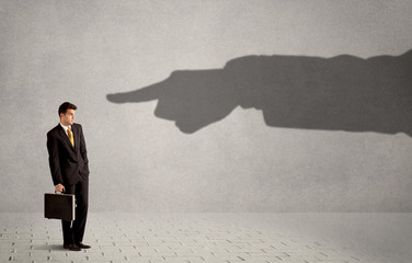 Business person looking at huge shadow hand pointing at him conc