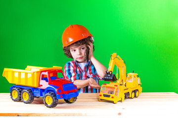 Plakat Little curly foreman talking on the phone, playing with trucks and excavators. Close-up. Green background.