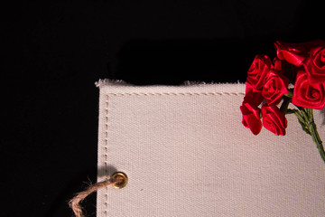 Red ribbon roses on the white textile covered notebook in black background
