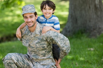 Portrait of army soldier giving piggyback ride to boy in park