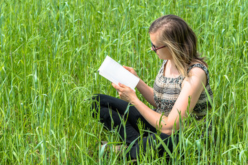 Young woman reading a book in the grass on spring meadow