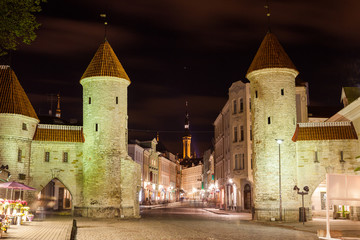 Fototapeta na wymiar Guard towers of Viru Gate, Narrow street illuminated of Old Town at night, City Hall on the background, Tallinn, Estonia