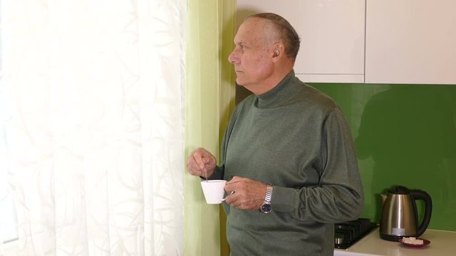 Aged man looking at the window with tea cup in his hands