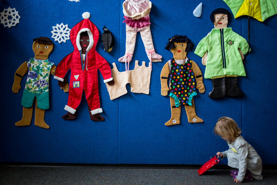 Young child crouching next to wall clad with clothes