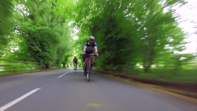 A stabilised view of a group of cycling athletes out on a training ride on country roads in the UK countryside on a sunny day. 