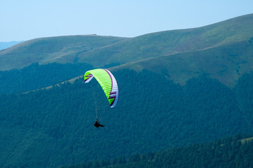 Paraglider flies paraglider over the tops of the mountains in summer sunny day. Carpathians, Ukraine.