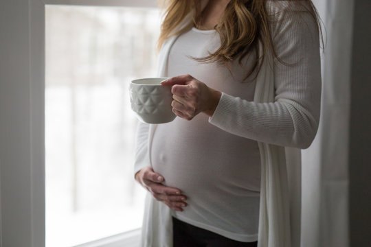 Pregnant woman holding tummy and cup 