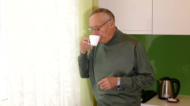 aged man standing near the window with the cup of tea