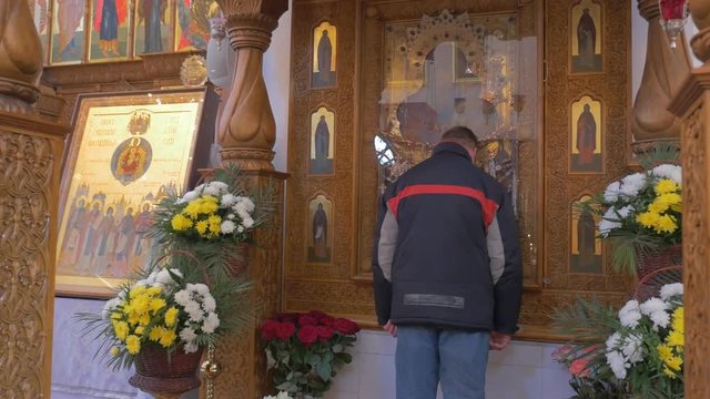 Religious Man Kisses an Ancient Icon of Saint Mary, Which is Covered With Glass and Has Two Carved Wooden Columns Before it