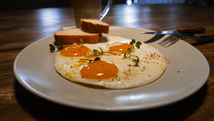 Fried eggs with bacon in a plate on a wooden table, selective focus, side angle view