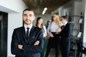 Young manager in front of his coworkers with crossed hands in modern office.