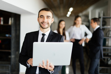 Business man with laptop in hands in front of discussing colleagues in office.