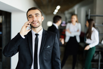 Business man speak on mobile phone in front of discussing colleagues in office.