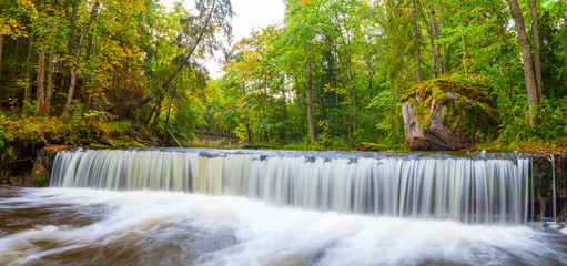 Small waterfall (cascade) on river with big stone, motion blur. Lahemaa national park, Estonia