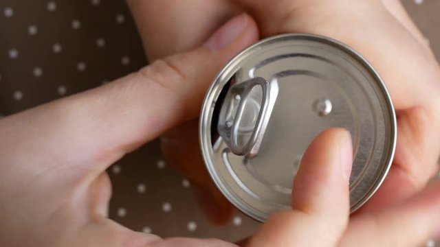 Top view of hand opening food tin can with tomato puree inside.