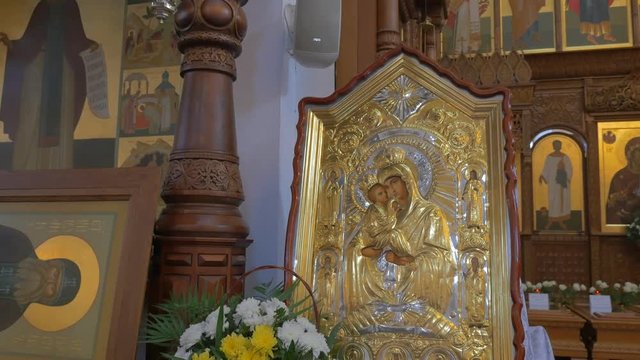 a Beautiful Saint Mary Icon in Orthodox Church, Covered With Glass and a Small Carved Wooden Roof and Several Praying People Standing Nearby