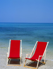 Zwei rote Liegestühle am menschenleeren Strand