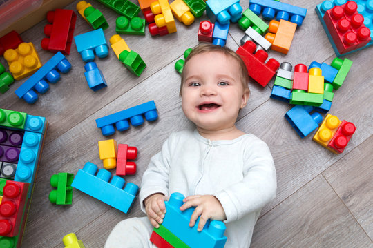 Little baby playing with lots of colorful plastic blocks constructor on floor in the room.