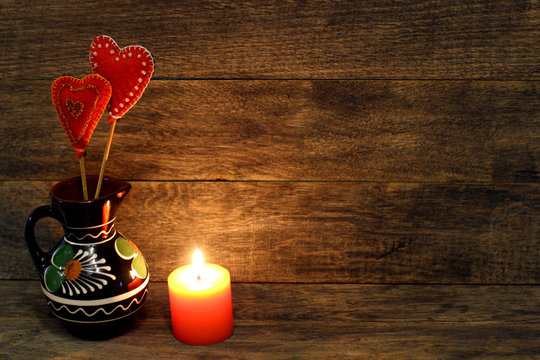 Decorative hand made hearts in small folk style vase and burning candle on wooden background. Sewed from a felt and decorated with beads. Card background for St. Valentine`s day. Copyspace.