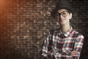 hipster style woman posing with crossed arms in front of a vintage brick wall