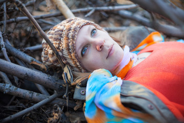 Attractive young woman laying down on the ground covered dry autumnal foliage in beautiful park and looking up in sky © Mykola Iegorov