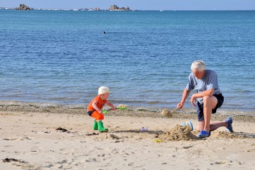 Un grand-père joue dans le sable avec son petit-fils sur une plage de Bretagne