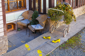 Beautiful terrace near handmade shop with flowers in carriage, chairs and funny yellow shoes