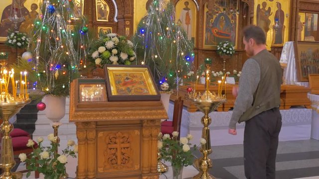 a Religious Man Prays Before a Jesus Christ Icon Inside of a Magnificent Orthodox Church With an Impressive Iconostasis and Decorated Fir Trees